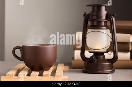 Braune Tasse Kaffee mit heißem Dampf, auf dem Schreibtisch mit Sonnenlichtlampe, grauer Hintergrund Stockfoto