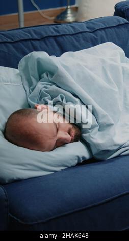 Nahaufnahme eines Erwachsenen mit Grippesymptomen, der auf dem Sofa liegt, um Erkältung und Viruserkrankungen zu heilen. Kranker Mann, der schläft und eine verschreibungspflichtige Behandlung hat, Pillen, Kapseln und Thermometer auf dem Tisch Stockfoto