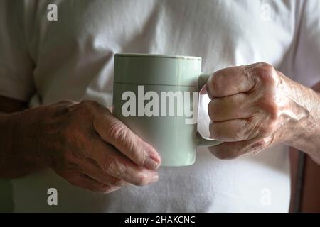 Älterer Mann mit einer Tasse heißem Getränk. Nahaufnahme seiner faltigen Hände. Stockfoto