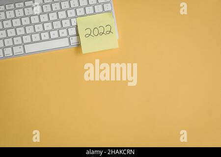 2022 auf gelbem Papierstift auf der Tastatur geschrieben. Draufsicht, Kopierbereich. Stockfoto