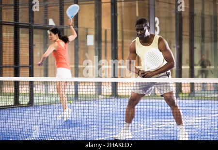 Fokussierter Afroamerikaner spielt ein freundliches Paddleball-Spiel auf einem kleinen geschlossenen Platz. Konzept der Konzentration im Wettbewerb. Stockfoto