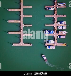 Luftaufnahme der Boote, die auf dem schwimmenden Pier angedockt sind. Ein Fischerboot fährt in den Hafen Stockfoto