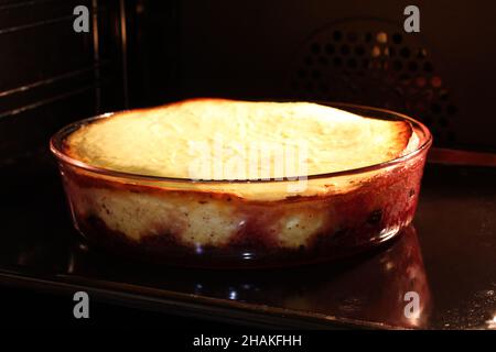 Im Ofen wird Quark-Auflauf mit Himbeeren und Haselnüssen in Glasform gebacken. Nahaufnahme. Stockfoto