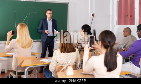 Professor für Mathematik hält Vorlesungen an Erwachsene Studenten im Auditorium, erklärt Funktionsdiagramm auf der Tafel Stockfoto