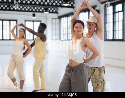 Junge Menschen üben Bachata-Tanzbewegungen paarweise während des Gruppenkurs im Proberaum Stockfoto