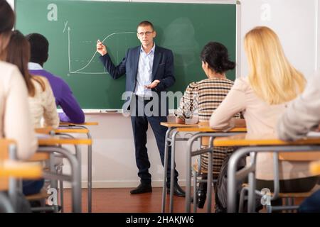 Positiver männlicher Dozent erklärt neues Thema in der Erwachsenenbildungsklasse Stockfoto