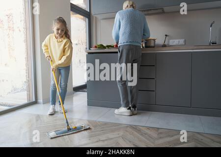 Fürsorgliches kleines Mädchen, das den Boden putzt, während es ihrer Großmutter hilft Stockfoto