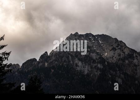 Graustufenaufnahme einer atemberaubenden Wolkenlandschaft über hohen felsigen Bergen an einem düsteren Tag Stockfoto