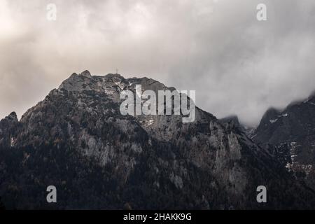 Graustufenaufnahme einer atemberaubenden Wolkenlandschaft über hohen felsigen Bergen an einem düsteren Tag Stockfoto