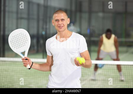 Porträt eines positiven Mannes mit Schläger und Ball in den Händen auf dem Padel Court Stockfoto