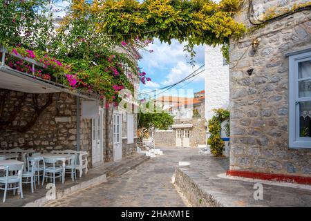 Eine malerische Straße aus Stein und weiß getünchten Häusern und ein kleines Café im Freien im Dorf der kleinen griechischen Insel Hydra, Griechenland. Stockfoto