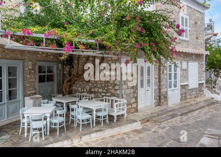Eine malerische Straße mit weiß getünchten Häusern und einem kleinen Café im Freien im Dorf der kleinen griechischen Insel Hydra, Griechenland. Stockfoto