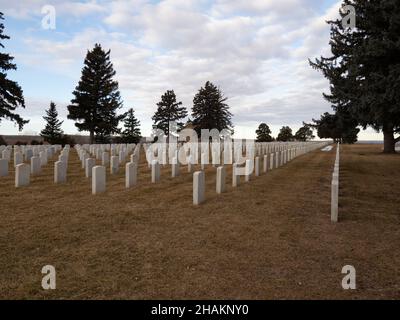 Reihen von Grabsteinen aus weißem Marmor auf dem Custer National Cemetery im Little Bighorn Battlefield National Monument in Montana. Das ursprüngliche Parkgebäude Stockfoto