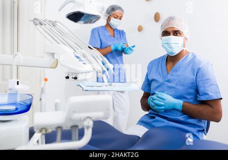 Qualifizierter Zahnarzt steht in blauer Uniform in der Zahnarztpraxis Stockfoto