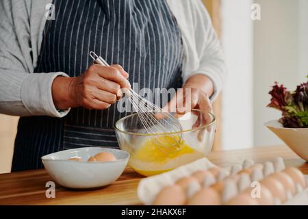 Nahaufnahme der Hände, ältere, multikulturelle weibliche Rühreier zum Frühstück. Im Ruhestand, gesund zu Hause. Stockfoto