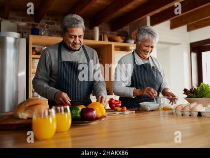 Glückliches multikulturelles älteres Paar, das in der modernen Küche Essen zubereitet. Essen gesunde Lebensmittel zu Hause, isoliert. Stockfoto