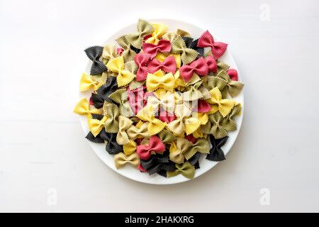 Mehrfarbige italienische rohe Pasta Nahaufnahme in einer Keramikplatte isoliert auf dem weißen Hintergrund Stockfoto