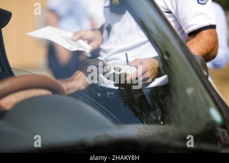 Highway 2 Bukarest - Constanta, Rumänien - 10. August 2021: Rumänischer Polizeibeamter übergibt einem Fahrer einen Alkoholtester, um seinen Alkoholgehalt zu testen. Stockfoto