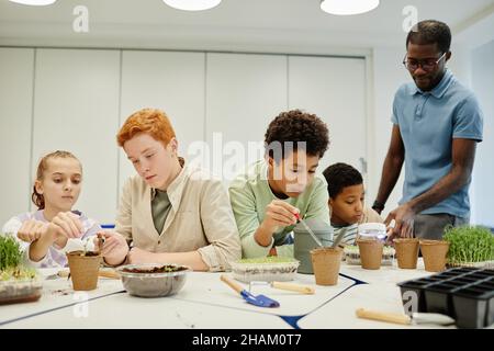 Eine vielfältige Gruppe von Kindern, die Samen Pflanzen, während sie in der Biologie in der Schule experimentieren Stockfoto