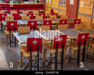 Gruyeres, Schweiz - 23. November 2021: Interieur eines typischen schweizer Restaurants in Gruyeres mit Stühlen mit schweizer Flagge auf der Rückseite. Stockfoto