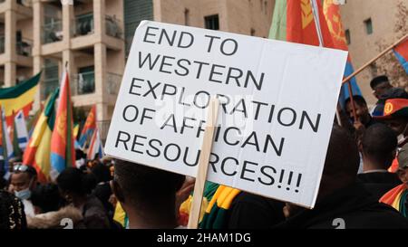 Jerusalem, Israel. 13h Dez 2021. Ein Protestierender hält ein Plakat mit der Aufschrift „Ende der westlichen Ausbeutung afrikanischer Ressourcen“ während eines Protestes, der von äthiopischen Juden und Mitgliedern der eritreischen Migrantengemeinschaft gegen die Politik der Vereinigten Staaten gegenüber dem Tigray-Konflikt Äthiopiens vor der US-Botschaft am 13. Dezember 2021 in Jerusalem, Israel, abgehalten wurde. Kredit: Eddie Gerald/Alamy Live Nachrichten Stockfoto