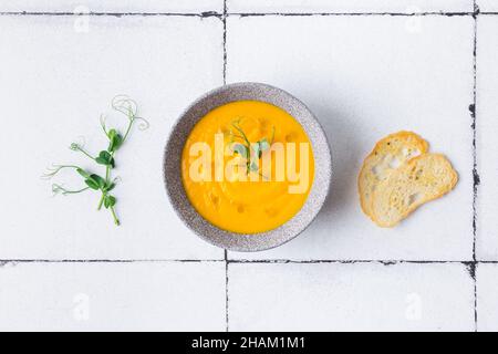 Kürbis- und Karottencremesuppe auf weißem Fliesenhintergrund mit Croutons. Draufsicht. Stockfoto