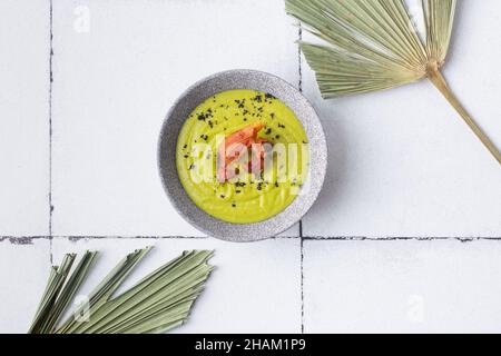 Grünes Suppenpüree mit gegrilltem Speck auf gefliesten Palmenblättern Stockfoto
