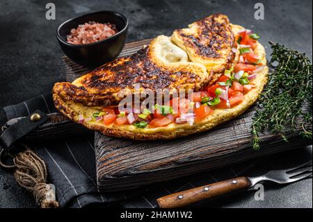 Gefülltes Omelett mit Tomaten, roter Paprika und Zwiebel auf Holzbrett. Schwarzer Hintergrund. Draufsicht Stockfoto