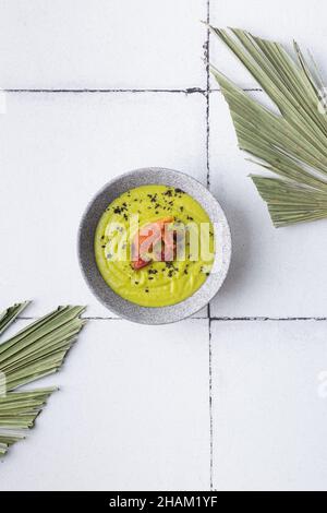 Grünes Suppenpüree mit gegrilltem Speck auf gefliesten Palmenblättern Stockfoto