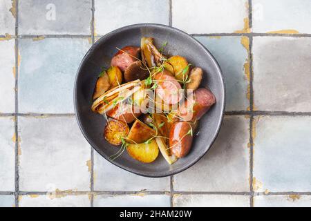 Gegrillte Würste mit Kartoffeln und Kräutern auf gefliestem Hintergrund. Fleisch. Draufsicht. Stockfoto