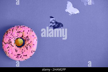 Pinkfarbener süßer Donut auf fliederfarbigem Hintergrund mit kleinen Schmetterlingen. Farbe des Jahres sehr peri Stockfoto