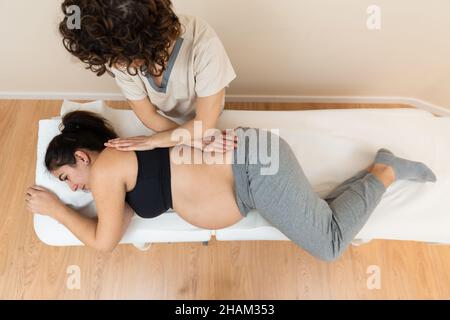 Physiotherapeutin, die eine auf der Seite einer Schwangeren auf einem Massageliegen in einem Gesundheitszentrum liegende Frau massiert Stockfoto