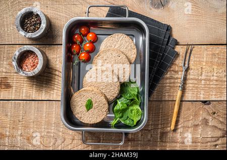 Rohe, fleischfreie Patties aus Fleisch auf pflanzlicher Basis, frische vegane Burger-Cutlets in Küchentablett mit Kräutern. Holzhintergrund. Draufsicht Stockfoto
