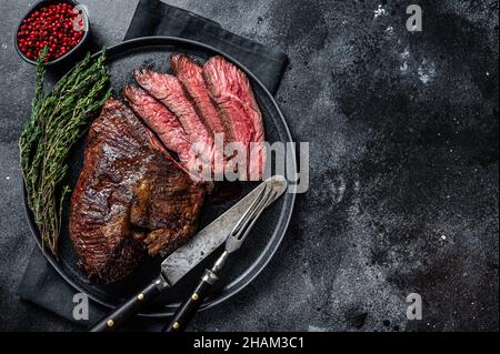 Gegrillter Aufhänger oder Onglet-Rindersteak auf einem Teller mit Thymian. Schwarzer Hintergrund. Draufsicht. Speicherplatz kopieren Stockfoto