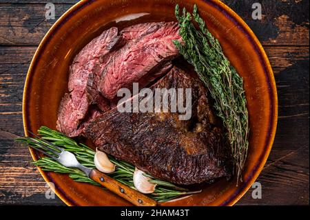 Gerösteter Aufhänger oder Onglet-Rinderfleischsteak in Scheiben auf einem rustikalen Teller mit Hackschnitzel. Dunkler Holzhintergrund. Draufsicht Stockfoto