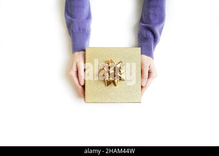 Hände in lila Pullover mit goldener Geschenkbox als Geschenk für Weihnachten, Neujahr, valentinstag oder Jubiläum auf weißem Hintergrund, Draufsicht. Stockfoto