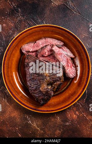 Gerösteter Aufhänger oder Onglet-Rinderfleischsteak in Scheiben auf einem rustikalen Teller mit Hackschnitzel. Dunkler Holzhintergrund. Draufsicht Stockfoto