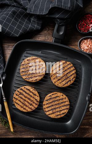 Gegrillte vegetarische Fleisch-Burger-Patties auf Pflanzenbasis, vegane Koteletts auf Grillpfanne. Holzhintergrund. Draufsicht Stockfoto