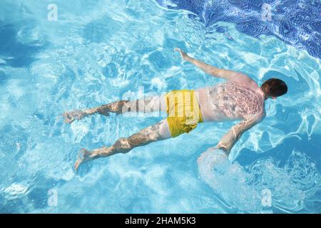 Männliche Person in Schwimmhosen schwimmend auf dem Wasser auf dem Bauch, klares Wasser im Pool Stockfoto