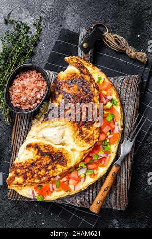 Gefülltes Omelett mit Tomaten, roter Paprika und Zwiebel auf Holzbrett. Schwarzer Hintergrund. Draufsicht Stockfoto