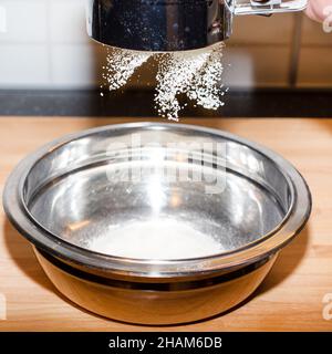 Sieben der weißen Blume durch ein Sieb in eine Metallschale Stockfoto