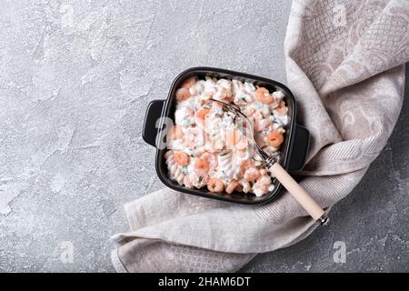 Draufsicht auf italienische Rotini-Pasta mit leckeren Garnelen in weißer cremiger Sauce auf grauem Beton-Hintergrund Stockfoto