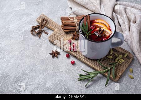 Traditionelles Herbstgetränk oder weihnachtsgetränk mit Orangen, Preiselbeere, Zimt, Rosmarin und anderen Zutaten auf grauem Betongrund Stockfoto