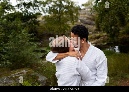 Junges Paar in Bademänteln, umarmt und küsst Stockfoto