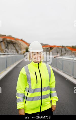 Porträt einer Ingenieurin in reflektierender Kleidung, die auf einer Brücke steht Stockfoto