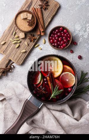 Traditionelles Herbstgetränk oder weihnachtsgetränk mit Äpfeln, Orangen, Preiselbeere, Zimt, Rosmarin und anderen Zutaten auf grauem Betongrund Stockfoto