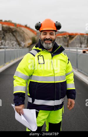 Porträt eines männlichen Ingenieurs in reflektierender Kleidung, die auf einer Brücke steht Stockfoto