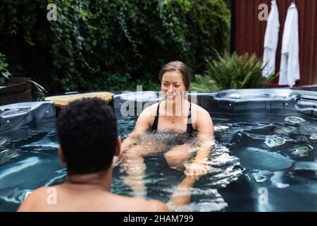 Lächelndes junges Paar, das im Whirlpool sitzt Stockfoto