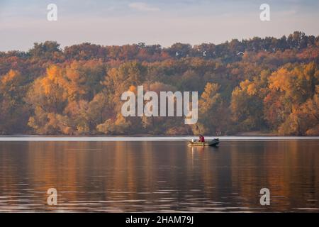 Grünes aufblasbares Gummimotorboot, das auf dem Fluss schwimmt, um auf dem Hintergrund herbstlicher Bäume zu fischen Stockfoto