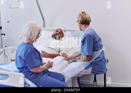 Mann im Krankenhausbett, der mit der Krankenschwester spricht Stockfoto